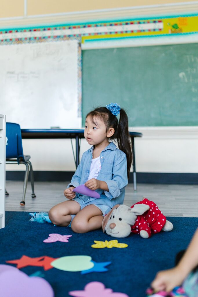Cute young girl in a preschool classroom playing with colorful toys on a carpet.