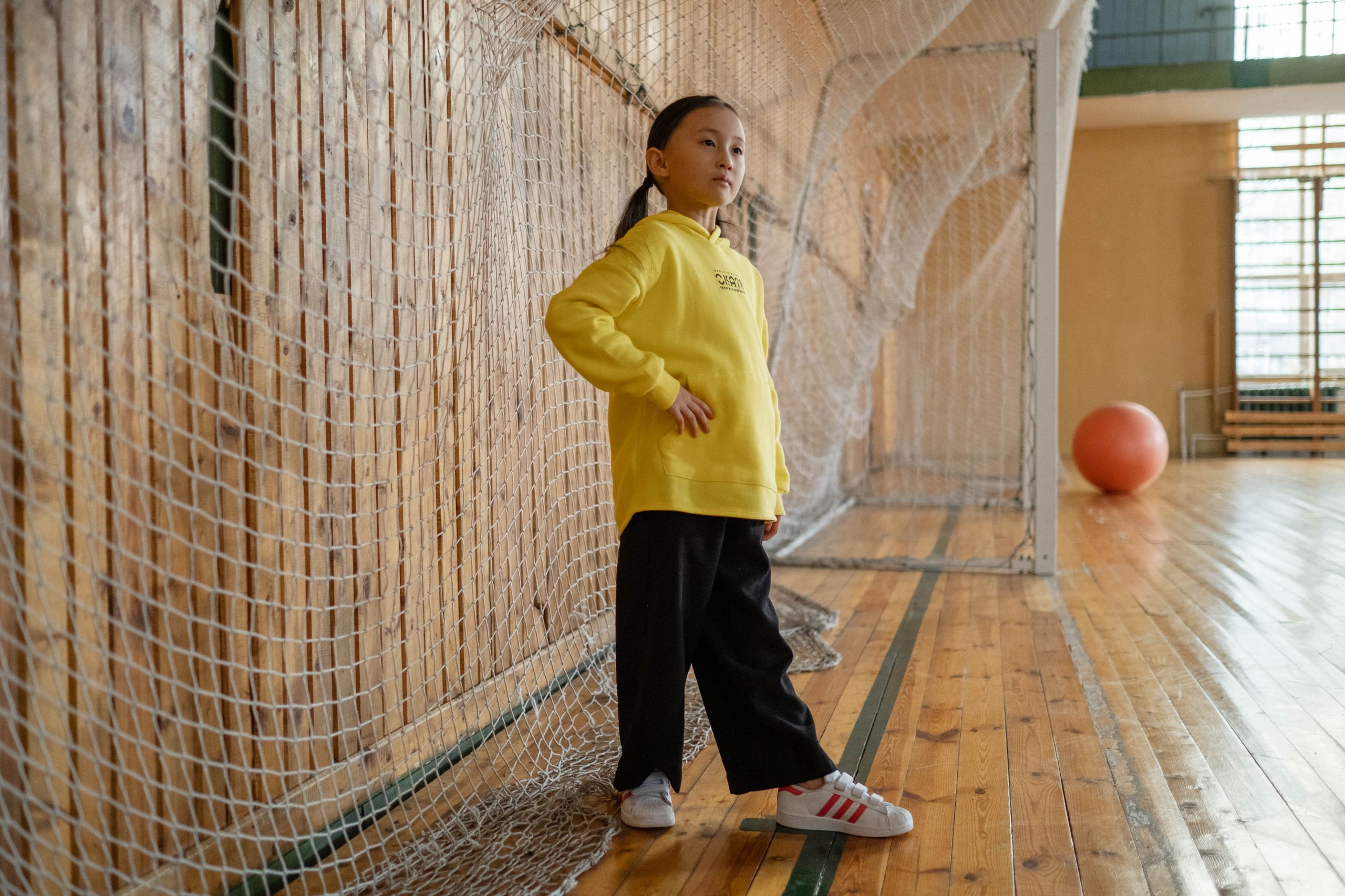 A young girl in a yellow jacket poses in a gym, showcasing sportswear fashion.